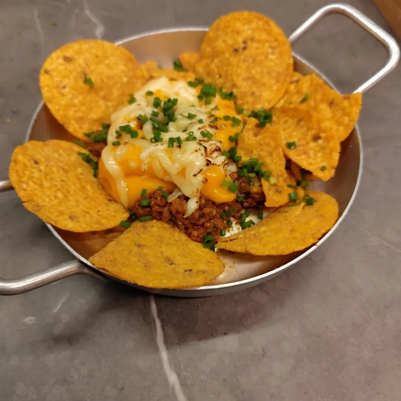 Nachos gratinados servidos na frigideira com molhos